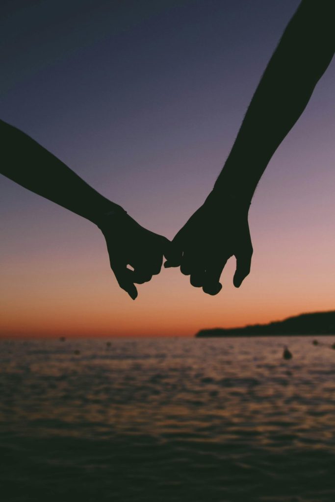 Silhouetted couple holding hands at sunset by the sea.